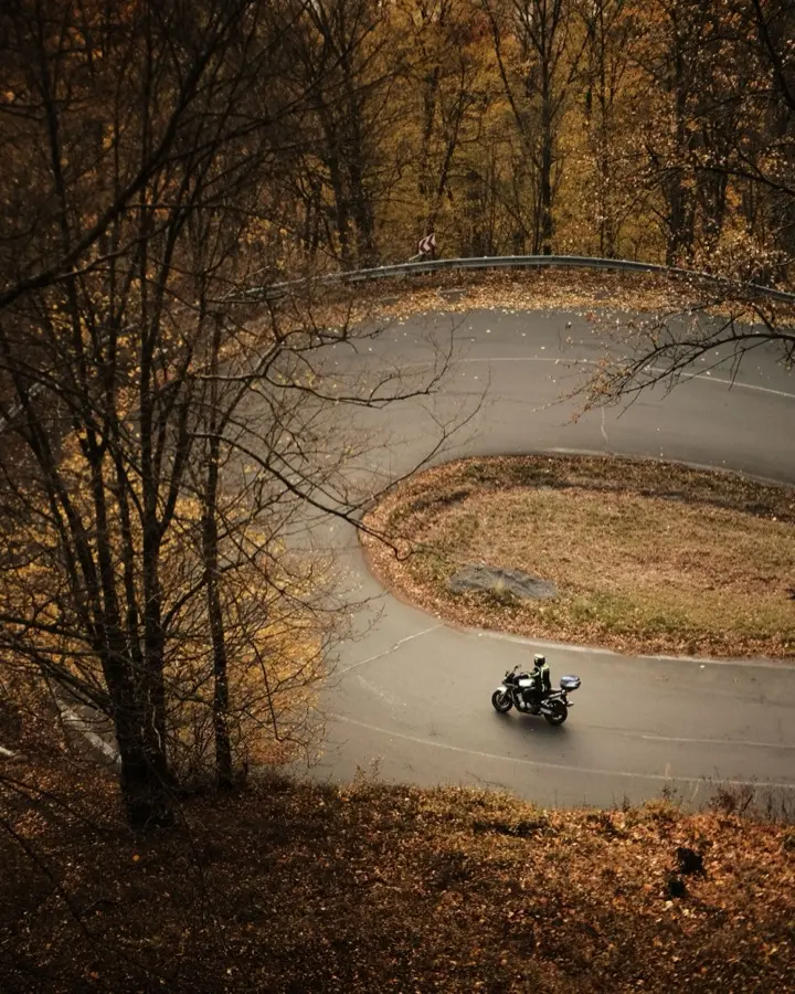 A motorcyclist rides through a hairpin bend in an autumn forest, seen from above
