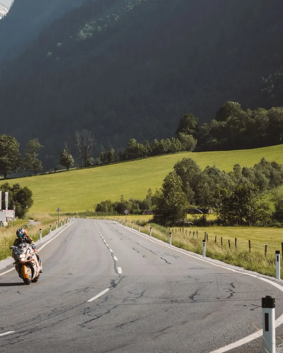 A lone motorcyclist on an alpine road, green meadows and steep mountains on both sides