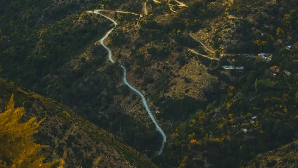 A narrow road winds through a mountain valley, seen from above